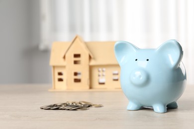 Photo of House model, piggy bank and coins on wooden table indoors, selective focus