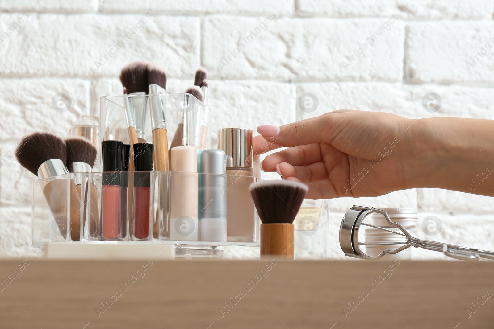 Photo of Woman taking cosmetics from organizer for makeup products on table