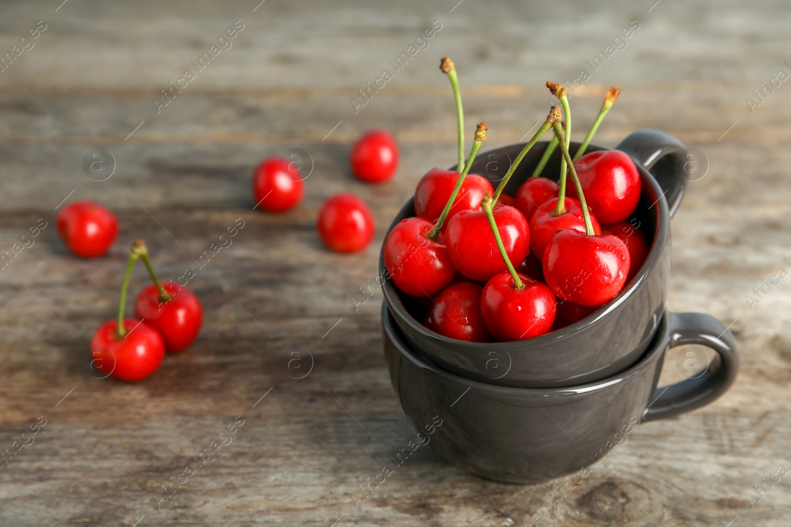 Photo of Cups with sweet red cherries on wooden table