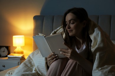 Woman with blanket reading book before bed at night