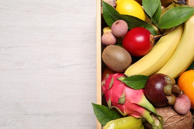 Photo of Crate with different exotic fruits on white wooden table, top view. Space for text