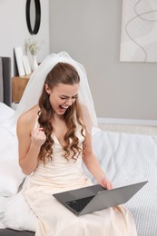Photo of Cheerful bride with laptop on bed in bedroom