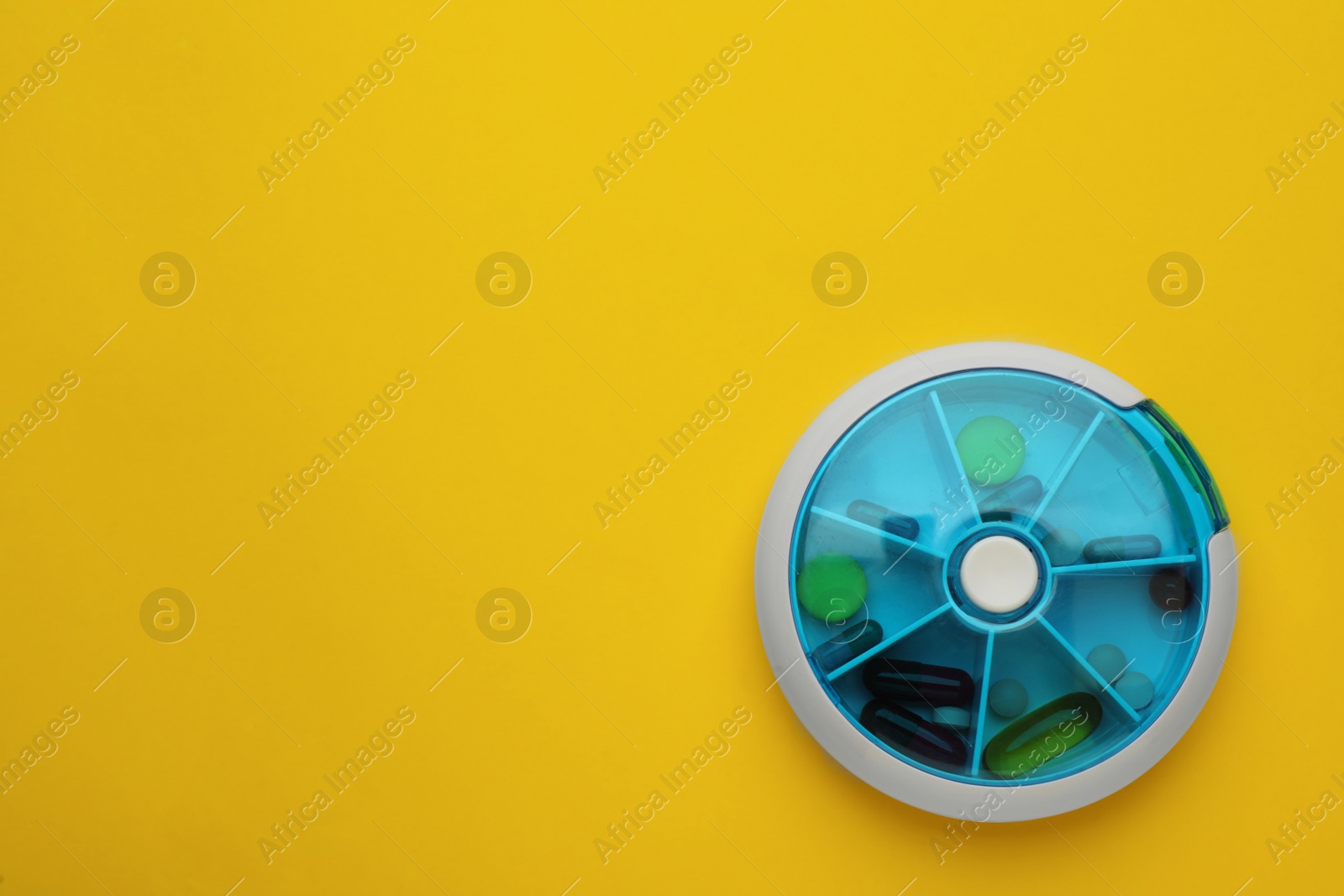 Photo of Plastic box with different pills on yellow background, top view. Space for text