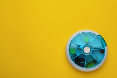 Plastic box with different pills on yellow background, top view. Space for text