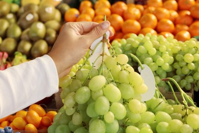 Woman holding fresh grapes near fruit counter at market, closeup