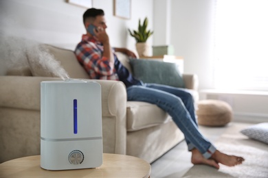 Photo of Modern air humidifier and blurred man on background