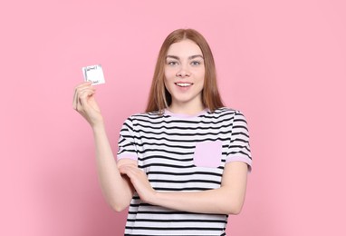 Woman holding condom on pink background. Safe sex