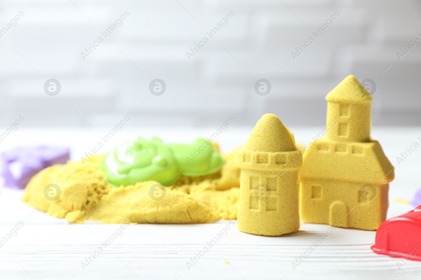 Photo of Castle figures made of yellow kinetic sand and plastic toys on white wooden table, closeup