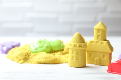 Castle figures made of yellow kinetic sand and plastic toys on white wooden table, closeup