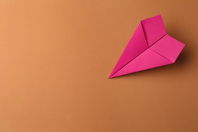 Handmade pink paper plane on brown background, top view. Space for text