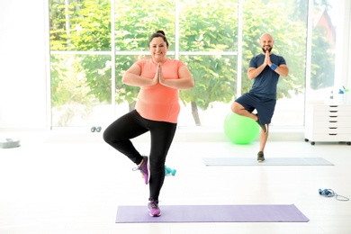 Overweight man and woman practicing yoga in gym