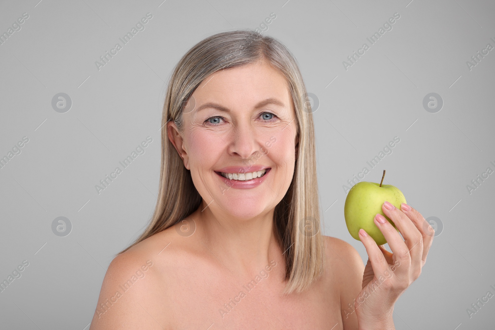Photo of Beautiful woman with fresh apple on grey background. Vitamin rich food