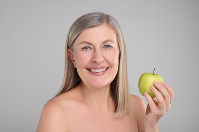 Photo of Beautiful woman with fresh apple on grey background. Vitamin rich food