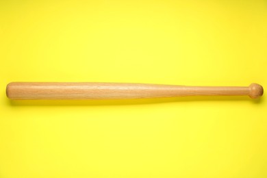 Photo of Wooden baseball bat on yellow background, top view. Sports equipment