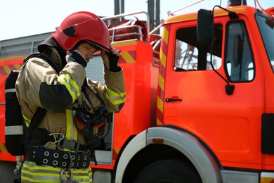 Photo of Firefighter in uniform wearing helmet near fire truck outdoors