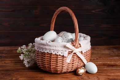 Photo of Wicker basket with festively decorated Easter eggs and white lilac flowers on wooden table