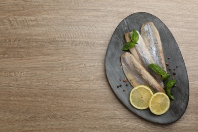 Photo of Delicious salted herring fillets served with lemon slices, peppercorns and basil on wooden table, top view. Space for text