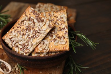 Photo of Cereal crackers with flax, sunflower, sesame seeds and rosemary on wooden table, closeup