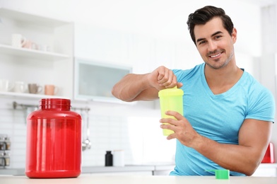 Photo of Young athletic man preparing protein shake in kitchen