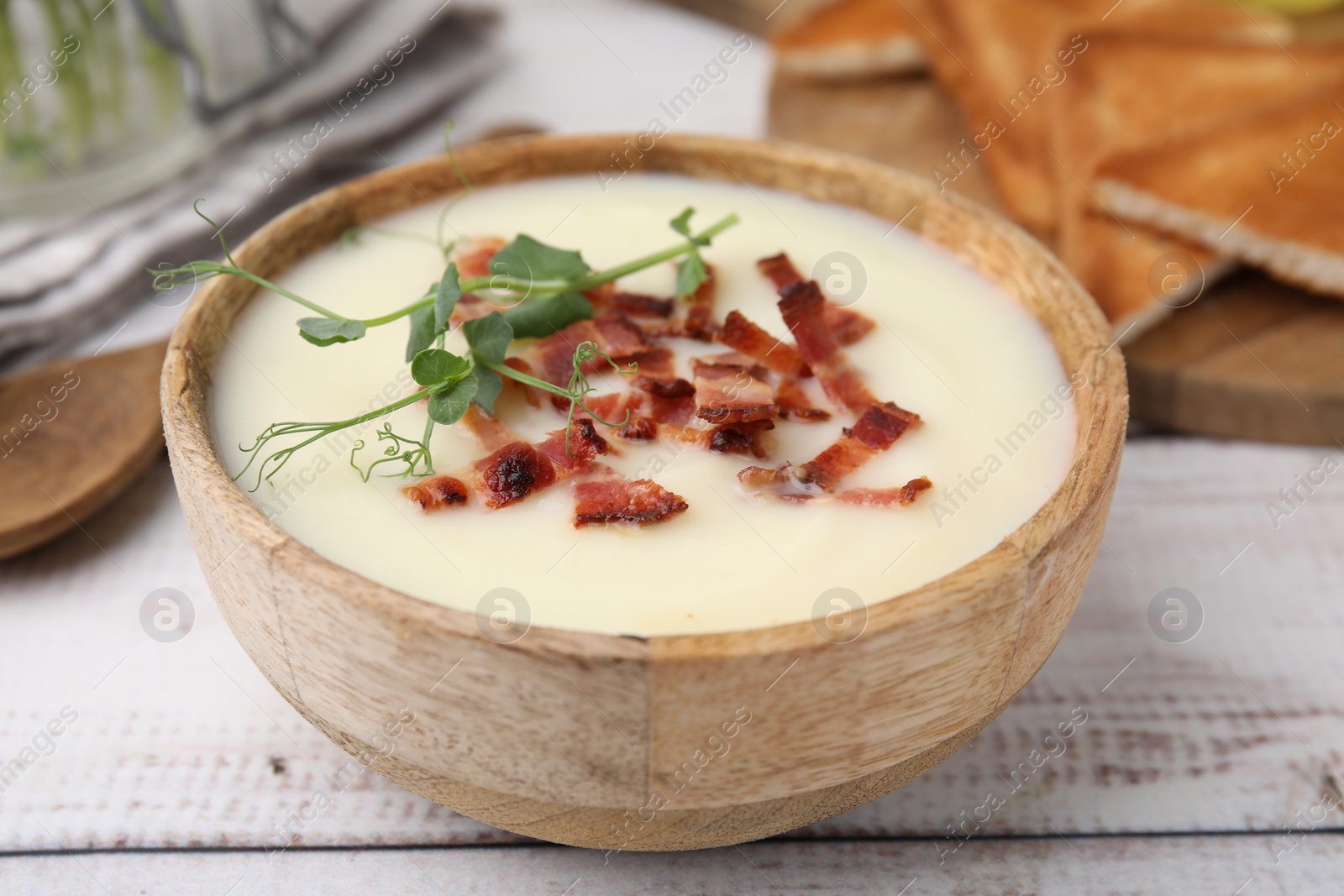 Photo of Delicious potato soup with bacon and microgreens in bowl on wooden table, closeup