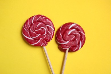 Sticks with bright lollipops on yellow background, flat lay