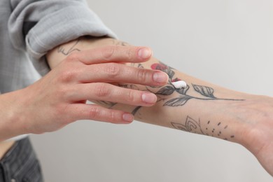 Photo of Tattooed woman applying cream onto her hand on light background, closeup