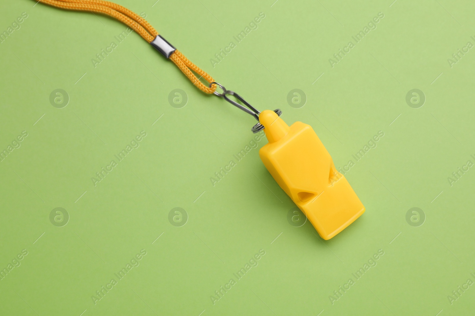 Photo of One yellow whistle with cord on light green background, above view