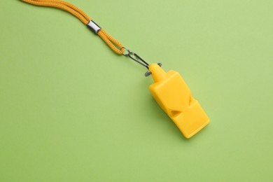 Photo of One yellow whistle with cord on light green background, above view