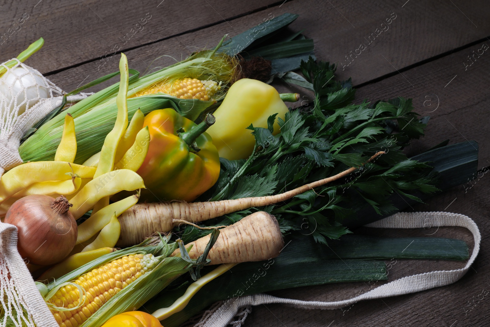 Photo of Different fresh ripe vegetables in net bag on wooden table, closeup