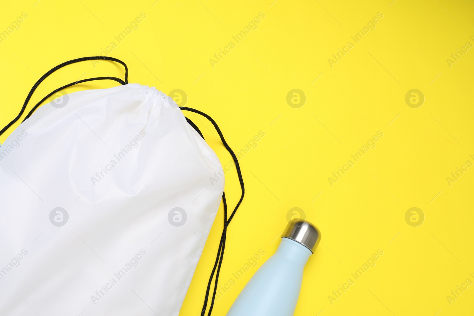 Photo of White drawstring bag and thermo bottle on yellow background, flat lay. Space for text