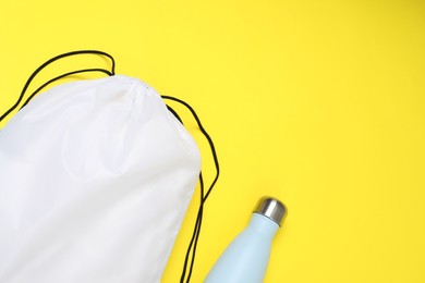 White drawstring bag and thermo bottle on yellow background, flat lay. Space for text