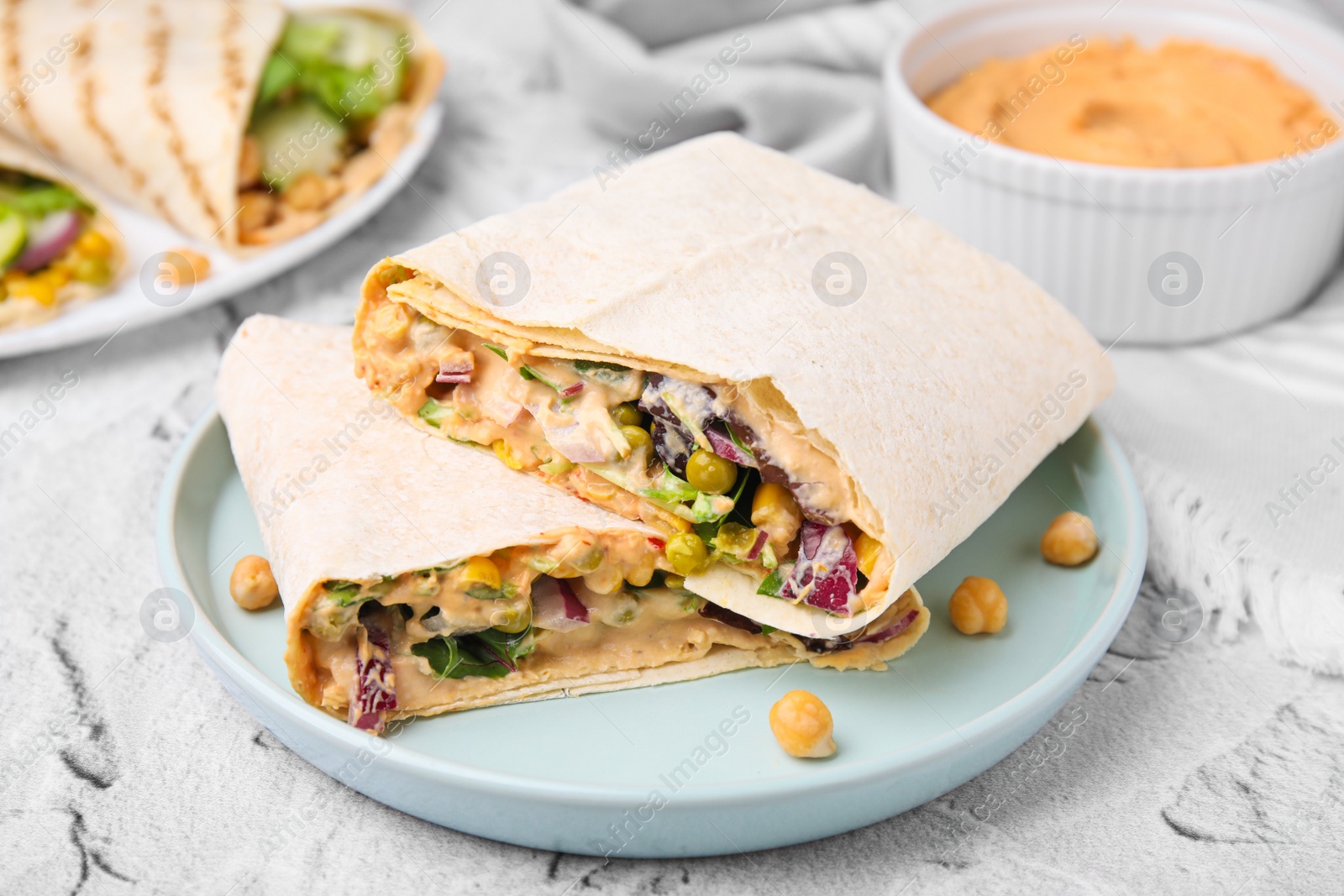 Photo of Delicious hummus wraps with vegetables on light grey textured table