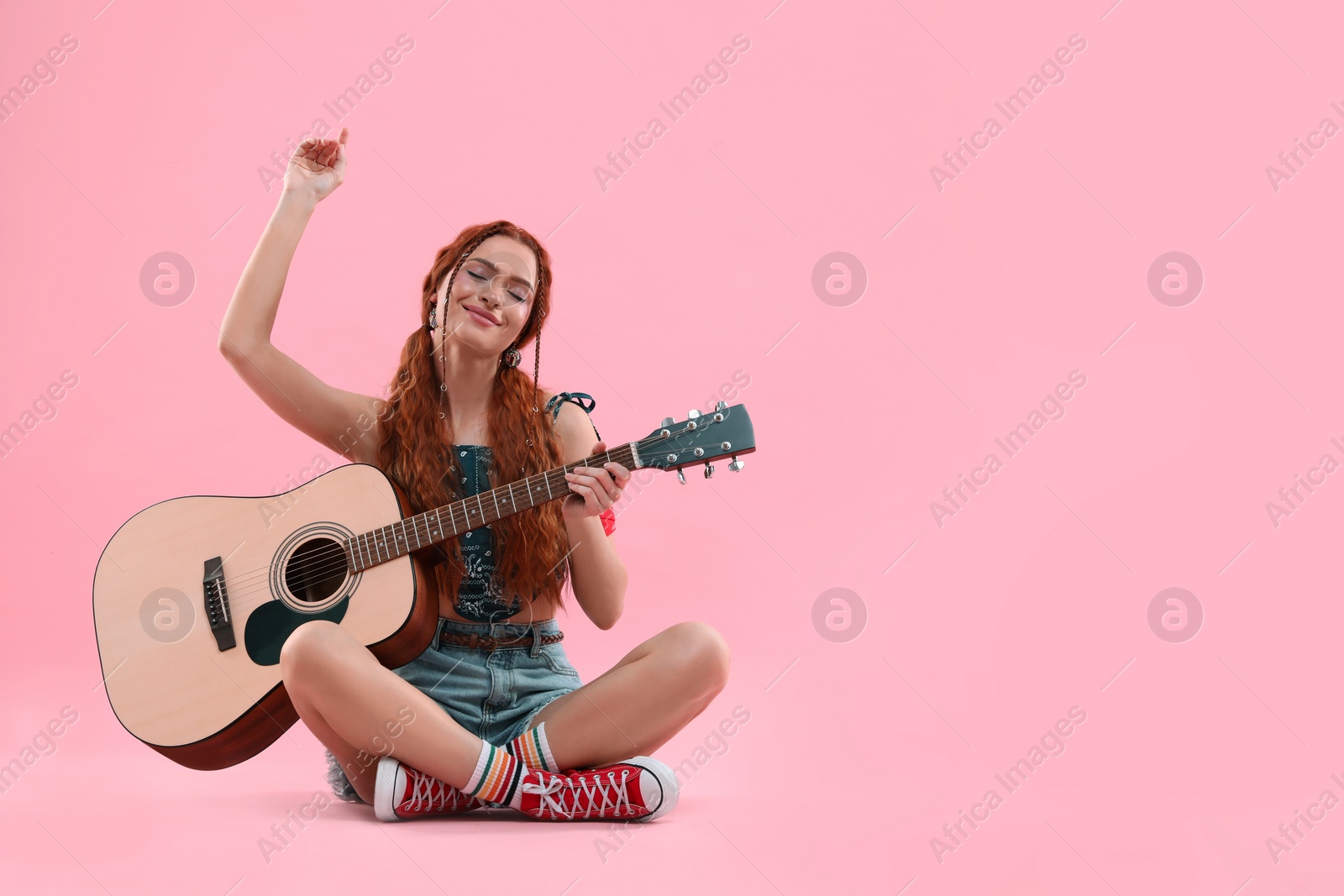 Photo of Stylish young hippie woman with guitar on pink background