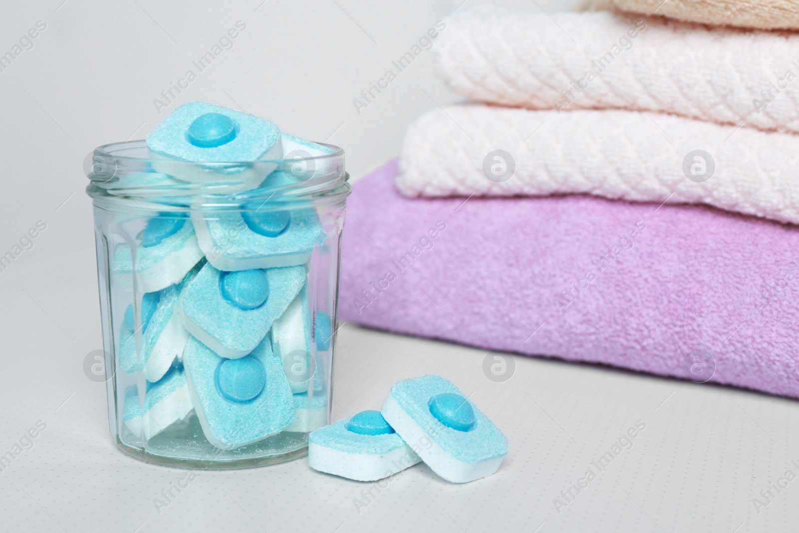 Photo of Jar with water softener tablets near stacked towels on white table