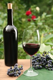 Photo of Red wine and grapes on wooden table outdoors