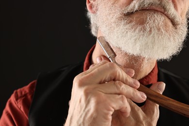 Man shaving beard with blade on black background, closeup