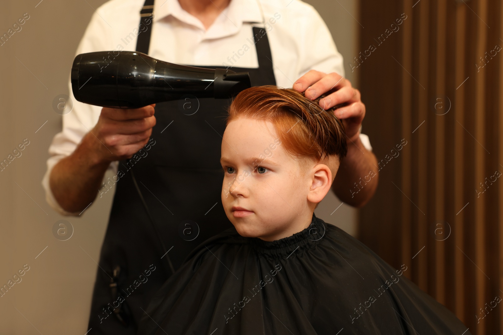 Photo of Professional hairdresser drying boy's hair in beauty salon