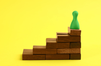 Photo of Green game piece on top of stairs against yellow background. Career promotion concept