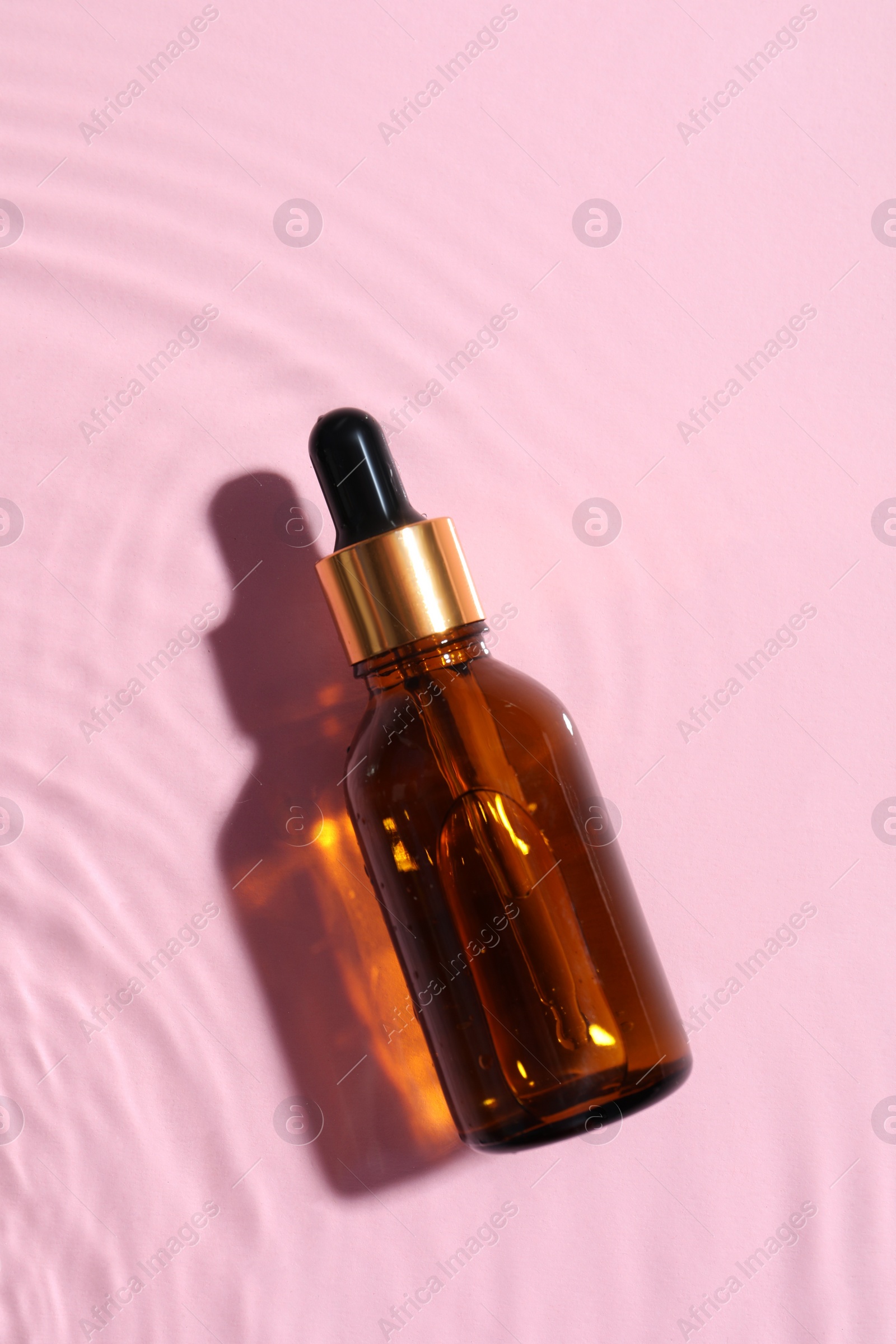 Photo of Bottle of cosmetic oil in water on pink background, top view