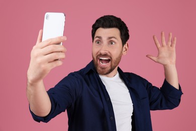 Surprised man taking selfie with smartphone on pink background