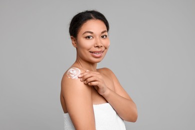 Photo of Young woman applying body cream onto shoulder on grey background