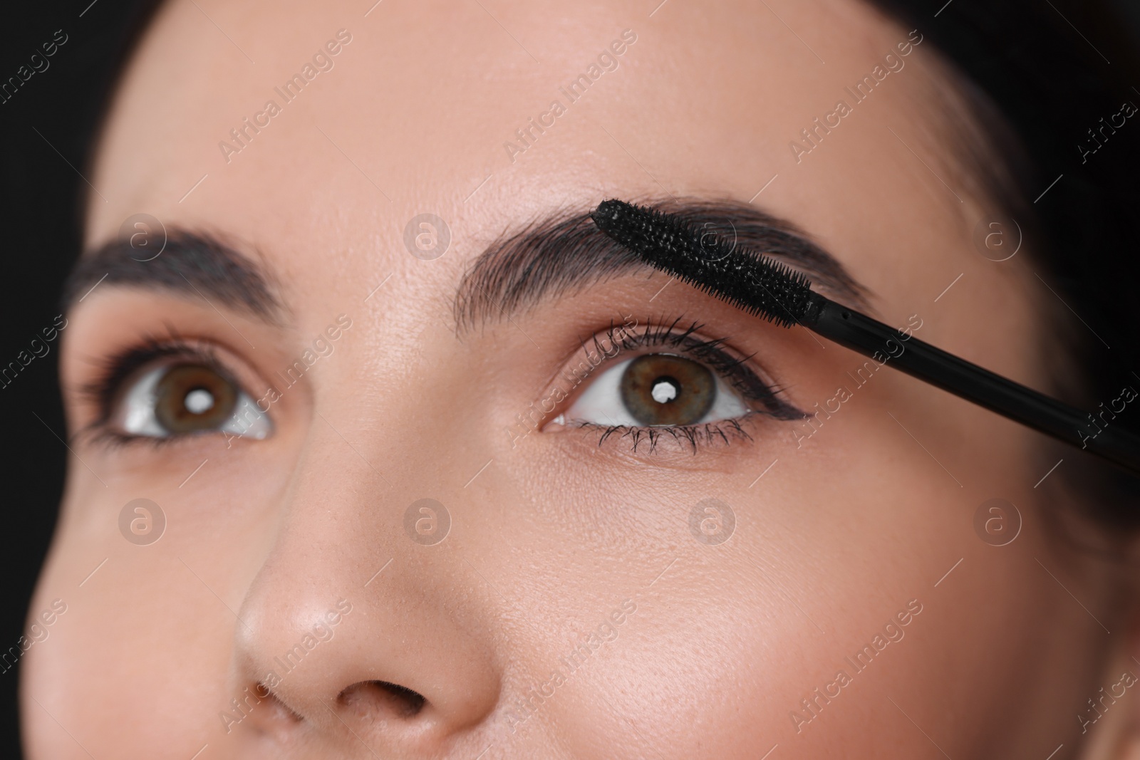 Photo of Beautiful young woman applying mascara on black background, closeup