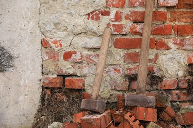 Sledgehammers near brick wall outdoors. Space for text