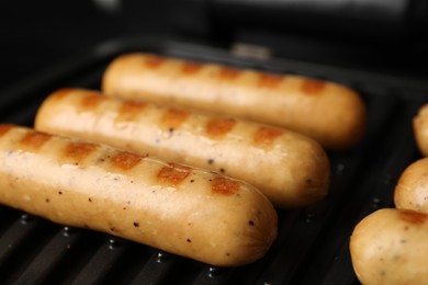 Delicious vegan sausages cooking on electric grill, closeup