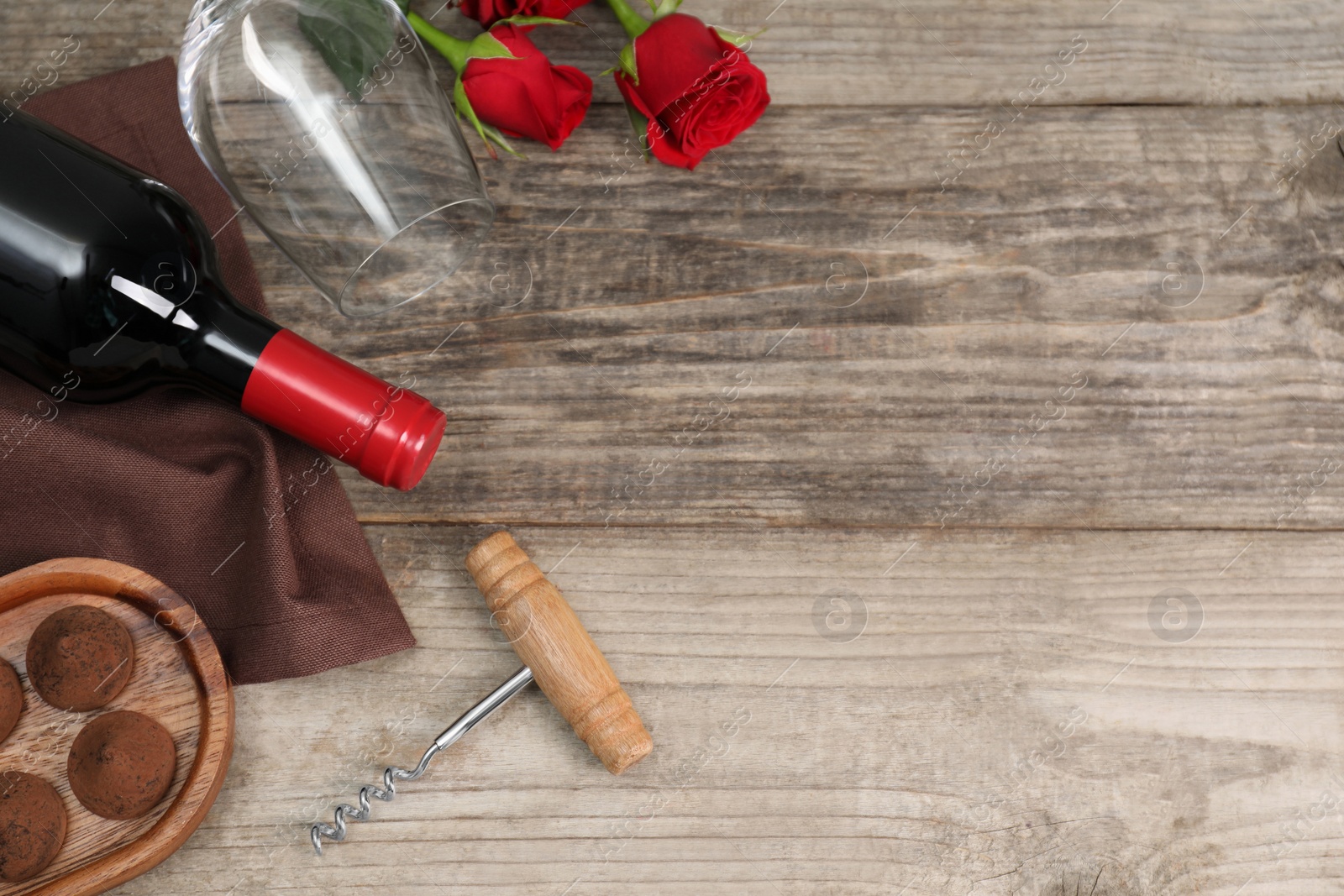 Photo of Bottle of red wine, glass, chocolate truffles, corkscrew and roses on wooden table, flat lay. Space for text