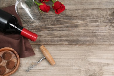 Photo of Bottlered wine, glass, chocolate truffles, corkscrew and roses on wooden table, flat lay. Space for text