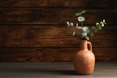 Photo of Beautiful eucalyptus branches in vase on wooden table indoors, space for text