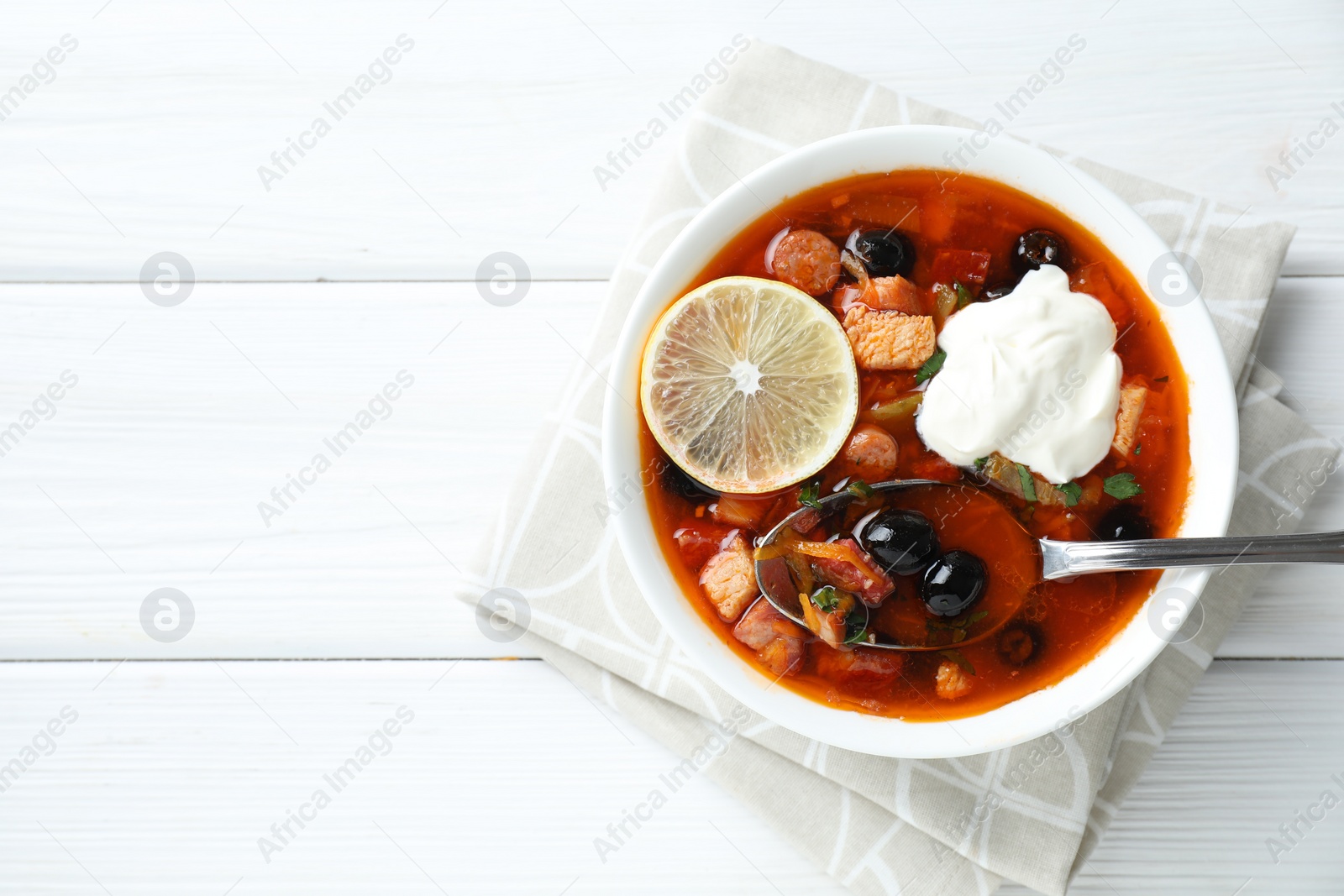 Photo of Meat solyanka soup with sausages, olives, vegetables and spoon on white wooden table, top view. Space for text