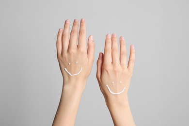 Photo of Smile painted with cream on hands against light grey background, closeup