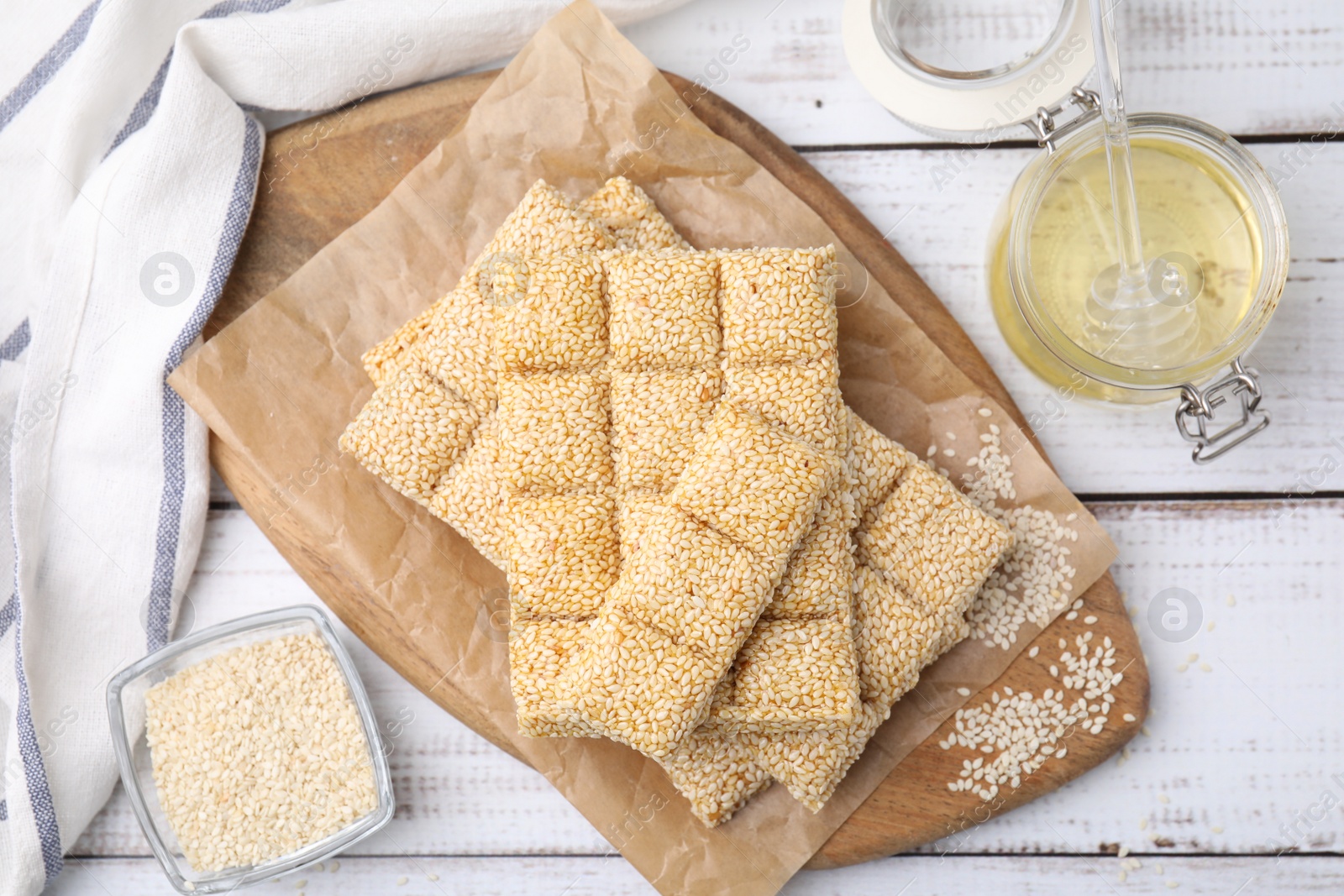 Photo of Delicious sweet kozinaki bars, sesame seeds and honey on white wooden table, flat lay